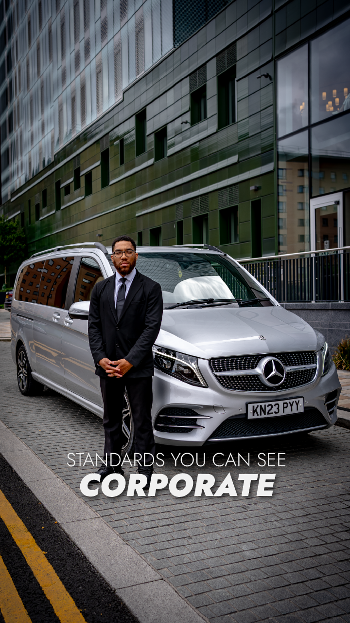 Chauffeur in black suit standing beside the V-Class outside a corporate building
